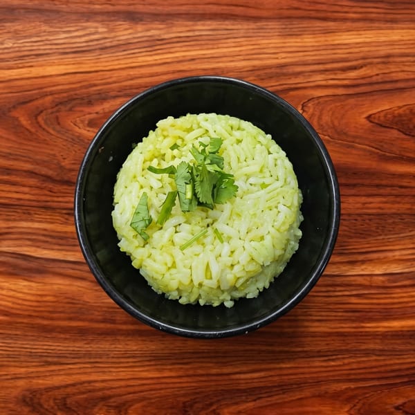 Green cilantro rice in a black bowl on a wooden table.