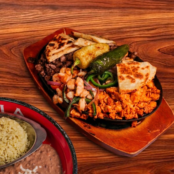 Sizzling fajita platter with chicken, shrimp, steak, peppers, onions, and quesadillas, with rice and beans.