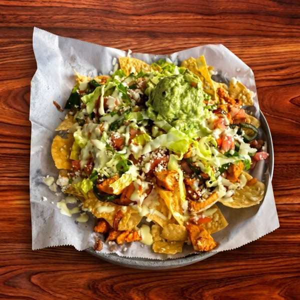 Loaded nachos with chicken, lettuce, tomatoes, cheese, and guacamole on a wooden table.